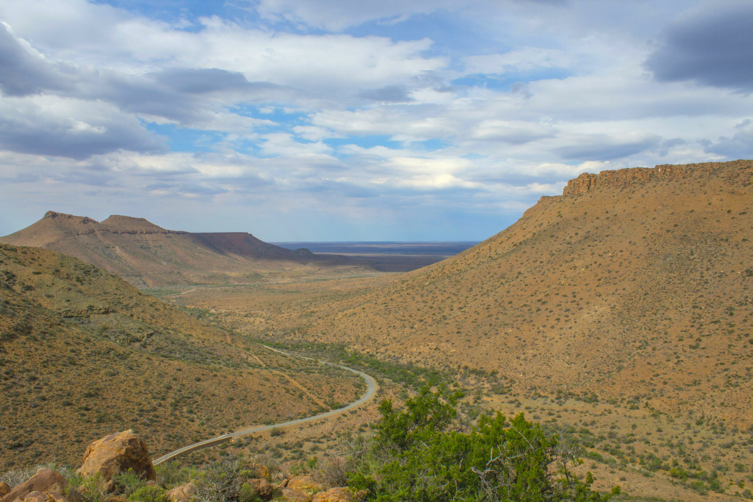 Das Bild zeigt Canyons in Afrika. Die Hänge sind trocken und felsig mit einigen Sträuchern. Im Tal verläuft eine Straße.